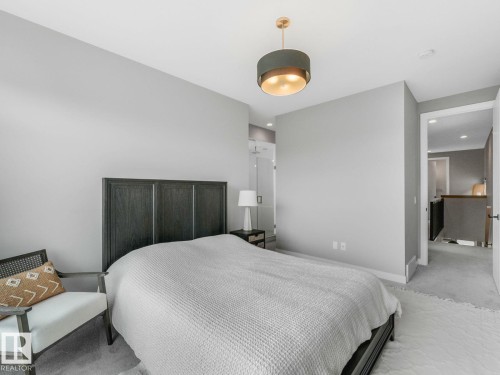 Spacious bedroom featuring light gray wall paint, gray carpet flooring, and a modern drum pendant light fixture with gold interior - 11613 72 Avenue Nw, Edmonton, AB - Indoor Photo Showing Bedroom