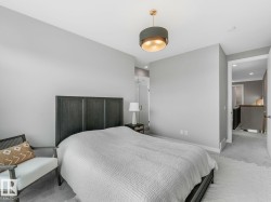 Spacious bedroom featuring light gray wall paint, gray carpet flooring, and a modern drum pendant light fixture with gold interior - 