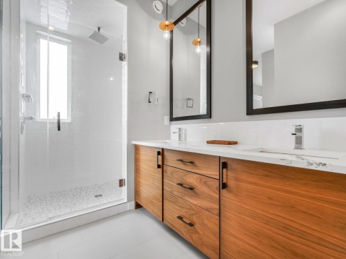 Modern bathroom featuring a wood-finish double vanity with stone countertops and undermount sinks - 11613 72 Avenue Nw, Edmonton, AB - Indoor Photo Showing Bathroom