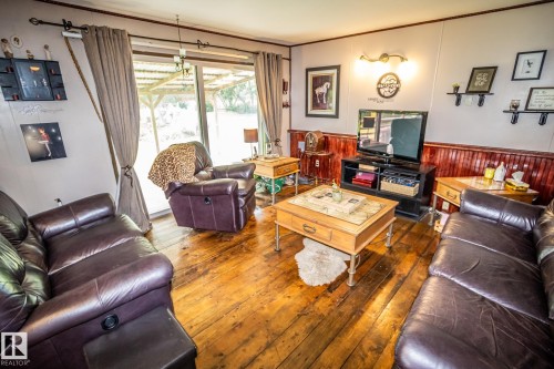Warm interior space featuring wood-finish flooring, a sliding glass door, and rich wood wainscoting - 11218 Twp Rd 590, Rural St. Paul County, AB - Indoor Photo Showing Living Room