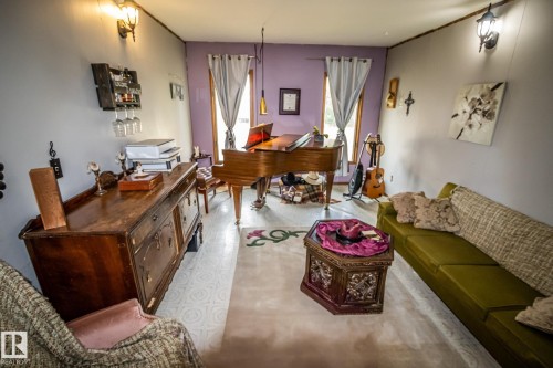 Spacious room featuring light-toned flooring, dual wall sconces, and a large window with drapes - 11218 Twp Rd 590, Rural St. Paul County, AB - Indoor Photo Showing Living Room