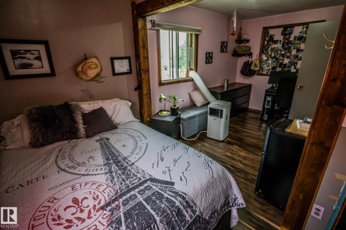 Bedroom featuring a wood post bed frame, wood-finish flooring, and soft mauve wall paint - 11218 Twp Rd 590, Rural St. Paul County, AB - Indoor Photo Showing Bedroom