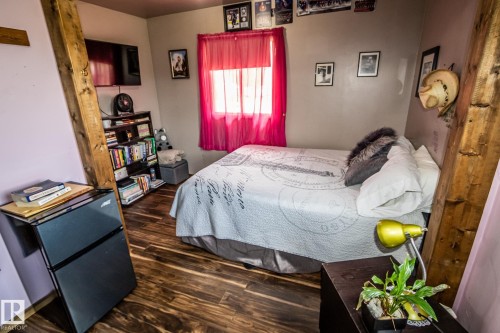 Cozy bedroom featuring wood-finish flooring, a comfortable bed with quality linens, and bright natural light from a red-curtained window - 11218 Twp Rd 590, Rural St. Paul County, AB - Indoor Photo Showing Bedroom