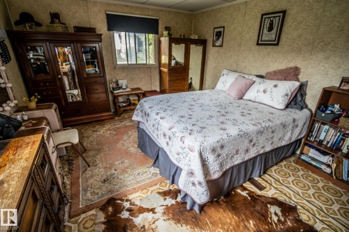 Bedroom featuring wood-finish flooring, a built-in wooden bookshelf, and a window with a roller shade - 11218 Twp Rd 590, Rural St. Paul County, AB - Indoor Photo Showing Bedroom