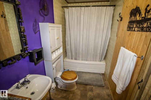 Bathroom featuring a white bathtub, a toilet with a wood-finish seat, a white pedestal sink with chrome fixtures, and a white storage cabinet - 11218 Twp Rd 590, Rural St. Paul County, AB - Indoor Photo Showing Bathroom