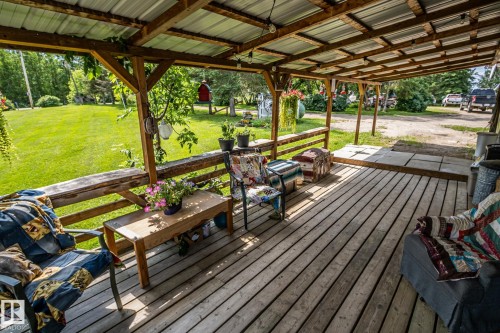 Expansive covered porch featuring wood-finish decking, exposed wood beam framing, and a corrugated metal roof - 11218 Twp Rd 590, Rural St. Paul County, AB - Outdoor With Deck Patio Veranda With Exterior