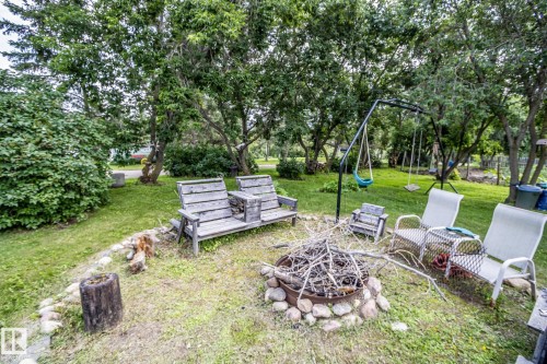 Expansive green space featuring a built-in fire pit with stone surround, mature trees, and a swing set - 11218 Twp Rd 590, Rural St. Paul County, AB - Outdoor