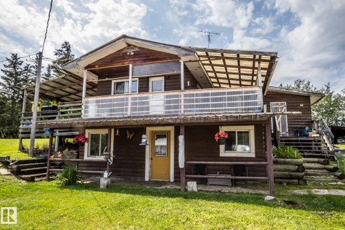 Two-story log cabin style residence featuring a covered upper-level balcony, a lower-level covered patio, and a bright yellow entry door - 11218 Twp Rd 590, Rural St. Paul County, AB - Outdoor
