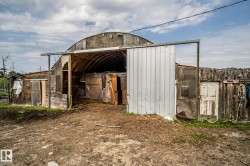 Quonset hut structure featuring a corrugated metal sliding door, exterior wooden siding, and a partial view of a metal fence - 