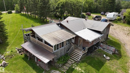 Expansive residential compound featuring a multi-section metal roof with modern standing seam panels, wraparound decking with multiple access points, and substantial covered porches - 11218 Twp Rd 590, Rural St. Paul County, AB - Outdoor With Deck Patio Veranda