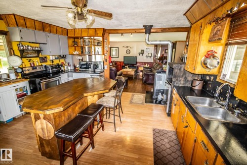 Kitchen featuring a wood-finish peninsula with seating, light wood-finish flooring, two-tone cabinetry, and a double stainless steel sink - 11218 Twp Rd 590, Rural St. Paul County, AB - Indoor