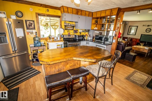Open-concept kitchen and dining area featuring a custom wood dining table, wood-finish flooring throughout, and stainless steel appliances - 11218 Twp Rd 590, Rural St. Paul County, AB - Indoor Photo Showing Dining Room