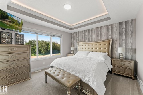 Recessed tray ceiling with integrated lighting, wood-finish accent wall, large picture windows, and soft neutral carpeting - 12383 176 Avenue Nw, Edmonton, AB - Indoor Photo Showing Bedroom