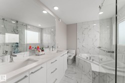 Bathroom featuring a dual vanity with undermount sinks, a corner soaking tub, and a separate glass-enclosed shower - 