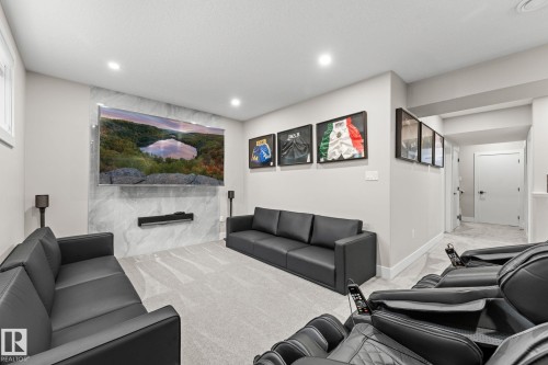 Spacious entertainment room featuring a large mounted screen, gray patterned carpet, recessed lighting, and a stone-look accent wall - 12383 176 Avenue Nw, Edmonton, AB - Indoor Photo Showing Living Room