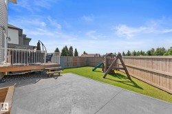 Expansive backyard featuring a concrete patio, wood deck with white railings, and a wooden privacy fence - 