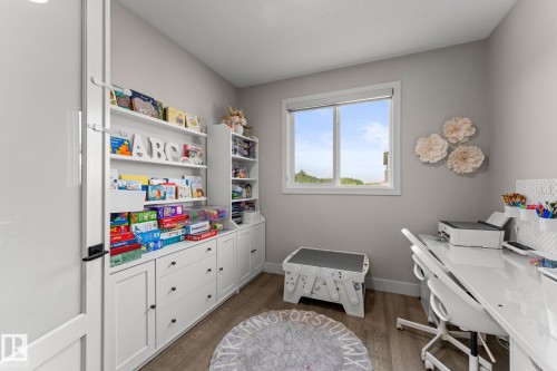 Room featuring built-in white cabinetry with varied storage options, a window, light gray wall paint, and wood-finish flooring - 12383 176 Avenue Nw, Edmonton, AB - Indoor Photo Showing Office