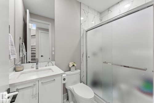 Modern bathroom featuring a floating vanity with an integrated sink and quartz countertop, chrome faucet and hardware, and a frameless glass shower enclosure with frosted panels - 12383 176 Avenue Nw, Edmonton, AB - Indoor Photo Showing Bathroom