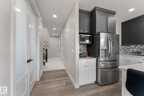 Modern kitchen featuring stainless steel appliances, dark upper cabinetry, white lower cabinetry, and a patterned tile backsplash - 12383 176 Avenue Nw, Edmonton, AB - Indoor