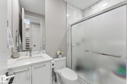 Modern bathroom featuring a floating vanity with an integrated sink and quartz countertop, chrome faucet and hardware, and a frameless glass shower enclosure with frosted panels - 