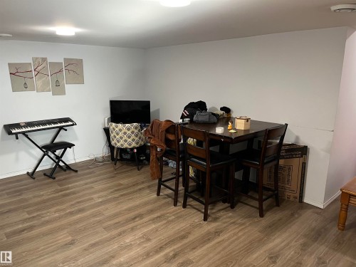 Versatile recreational space featuring wood-finish flooring, a dining table with seating for multiple guests, built-in shelving with storage capacity, and a keyboard instrument - 12011 87 Avenue Nw, Edmonton, AB - Indoor