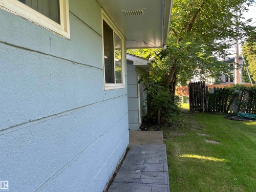 Side yard featuring a paved walkway with charcoal-toned pavers, mature landscaping with established greenery, privacy fencing, and lush lawn space - 12011 87 Avenue Nw, Edmonton, AB - Outdoor