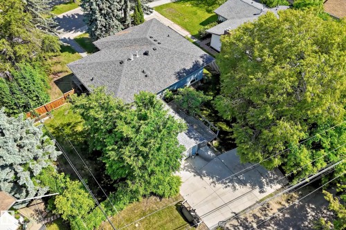 Property featuring a gray shingle roof, mature landscaping, a concrete driveway, a privacy fence, and a spacious green lawn - 12011 87 Avenue Nw, Edmonton, AB - Outdoor