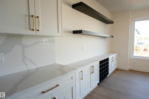 Built-in cabinetry with gold-finish hardware, light-toned countertops with distinctive veining, a dedicated wine rack, and complementary floating shelves - 34 Mckenzie Close Close, Leduc, AB - Indoor