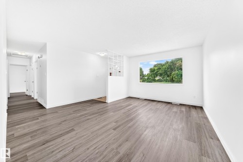 Spacious room featuring wood-finish flooring, white walls, and a large window overlooking lush greenery - 5519 142 Avenue Nw, Edmonton, AB - Indoor Photo Showing Living Room