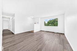 Spacious room featuring wood-finish flooring, white walls, and a large window overlooking lush greenery - 