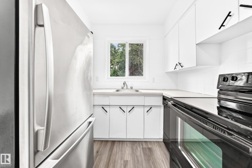 Kitchen featuring stainless steel refrigerator, white cabinetry with black hardware, black electric range, and wood-finish flooring - 5519 142 Avenue Nw, Edmonton, AB - Indoor Photo Showing Kitchen