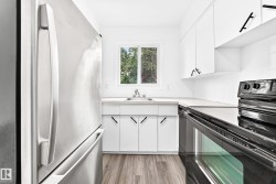 Kitchen featuring stainless steel refrigerator, white cabinetry with black hardware, black electric range, and wood-finish flooring - 