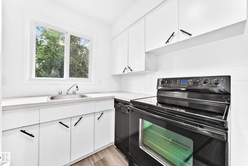 Kitchen featuring white cabinetry with matte black hardware, a stainless steel sink with a chrome faucet, light-toned countertops, and a black electric range with a visible oven - 5519 142 Avenue Nw, Edmonton, AB - Indoor Photo Showing Kitchen