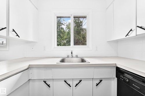 Bright kitchen featuring a stainless steel sink, white cabinetry with matte black hardware, white countertops, and a full-size black dishwasher - 5519 142 Avenue Nw, Edmonton, AB - Indoor Photo Showing Kitchen