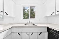 Bright kitchen featuring a stainless steel sink, white cabinetry with matte black hardware, white countertops, and a full-size black dishwasher - 