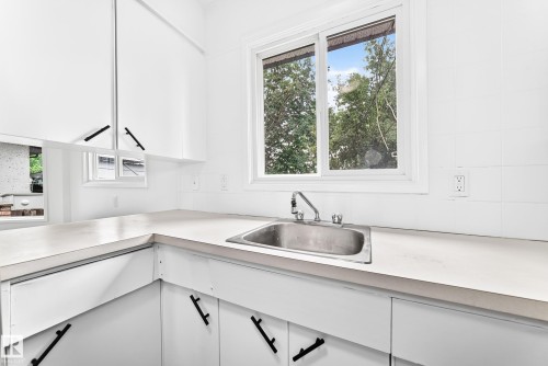Kitchen area featuring white cabinetry with black pulls, light-toned countertops, and a stainless steel sink with a chrome faucet - 5519 142 Avenue Nw, Edmonton, AB - Indoor Photo Showing Kitchen