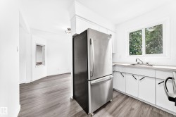 Kitchen area featuring wood-finish flooring, white cabinetry with black hardware, a stainless steel refrigerator, and a sink with a window overhead - 
