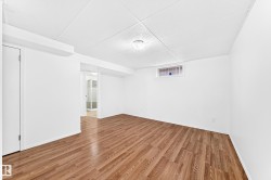 Spacious room featuring wood-finish flooring, white walls, and a drop ceiling with recessed lighting - 