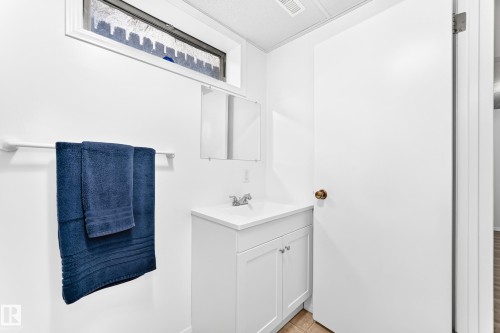Bathroom featuring a single vanity with storage, an integrated sink, a wall-mounted mirror, and a small transom window - 5519 142 Avenue Nw, Edmonton, AB - Indoor