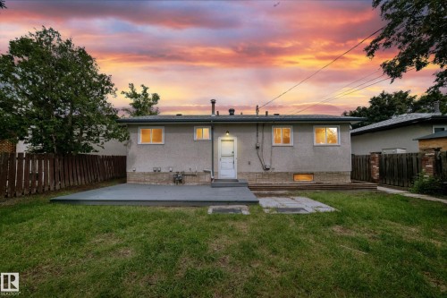Rear exterior featuring a stuccocoated facade, a ground-level patio, a separate stone paver area, a fenced perimeter, and mature trees - 5519 142 Avenue Nw, Edmonton, AB - Outdoor