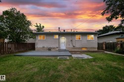 Rear exterior featuring a stuccocoated facade, a ground-level patio, a separate stone paver area, a fenced perimeter, and mature trees - 