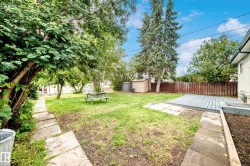 Expansive backyard featuring a large green lawn, mature trees, a wood deck, a storage shed, and a stone paver pathway - 