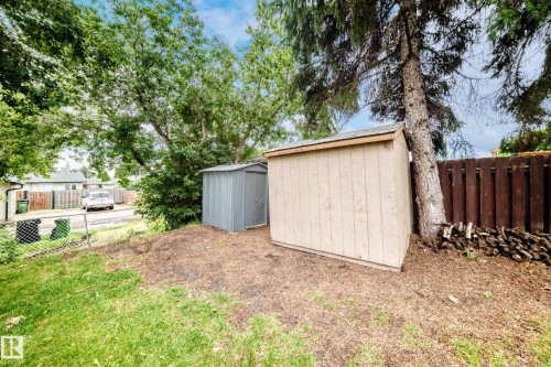 Two storage sheds on a partially mulched area, featuring a tall wooden fence and mature trees - 5519 142 Avenue Nw, Edmonton, AB - Outdoor