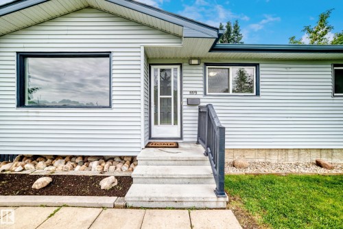 Exterior featuring light-colored siding, contrasting dark trim, and a prominent front entrance with a storm door - 5519 142 Avenue Nw, Edmonton, AB - Outdoor