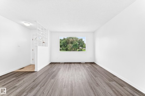 Expansive interior space featuring wood-finish flooring, white walls, and a large window - 5519 142 Avenue Nw, Edmonton, AB - Indoor