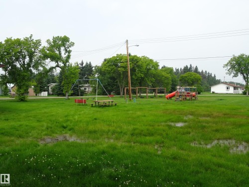 Expansive green space featuring multiple play structures including swings and a slide - 5140 51 Avenue, Vilna, AB 