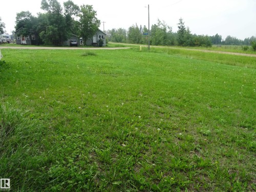 Expansive green lawn with visible road frontage and a distant wooded perimeter - 5140 51 Avenue, Vilna, AB 