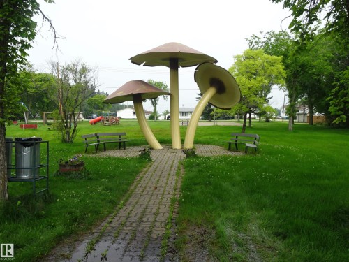 Expansive park area featuring three large mushroom sculptures on a paver base, surrounded by green lawns and mature trees - 5140 51 Avenue, Vilna, AB 