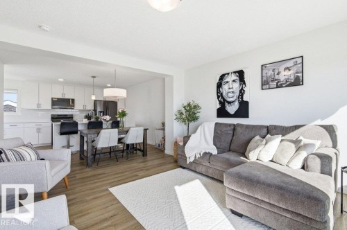 Open-concept living space featuring wood-finish flooring, a contemporary kitchen with white cabinetry, a kitchen island with seating, pendant lighting, and a drum pendant light fixture - #49 850 Secord Bv Nw, Edmonton, AB - Indoor Photo Showing Living Room