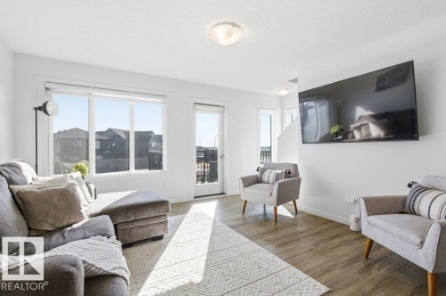 Bright living area featuring wood-finish flooring, white walls, and a large picture window - #49 850 Secord Bv Nw, Edmonton, AB - Indoor Photo Showing Living Room